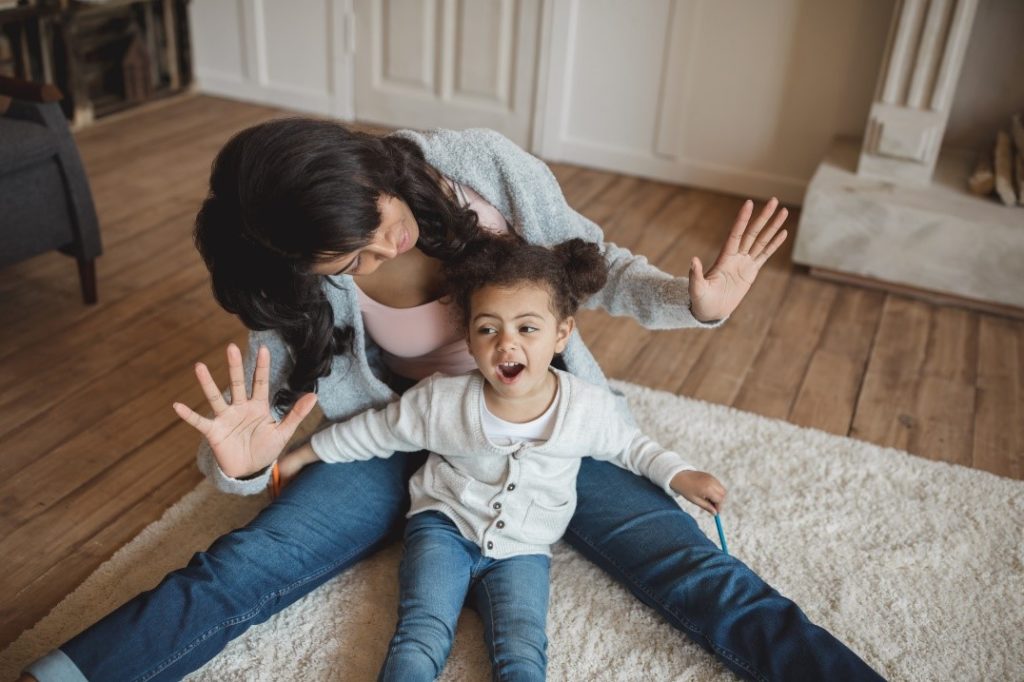mom with hands in air sitting on the floor with child